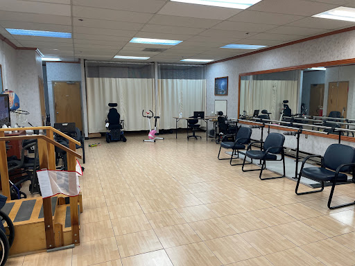An empty dance studio featuring mirrors, wooden flooring, and chairs arranged around the space.