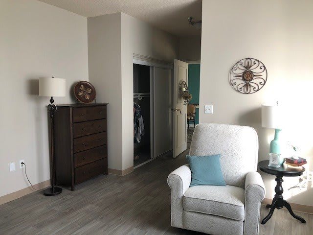 A cozy living room with an armchair, dresser, and wall clock.