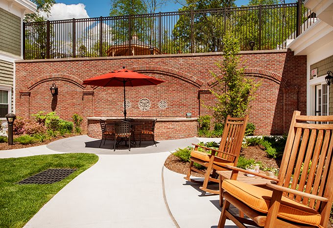 A cozy outdoor patio with wooden chairs and a red umbrella against a brick wall backdrop.