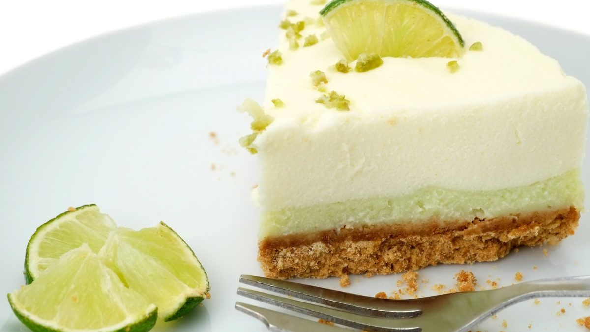 A slice of lime cheesecake with a crumbly crust on a plate, garnished with lime.