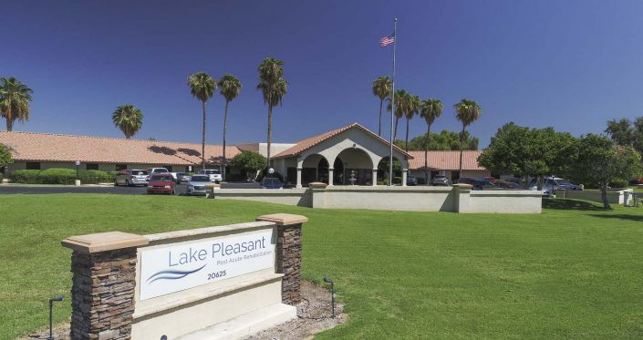 A sunny day at a building with palm trees and a manicured lawn, featuring a prominent sign in the foreground.