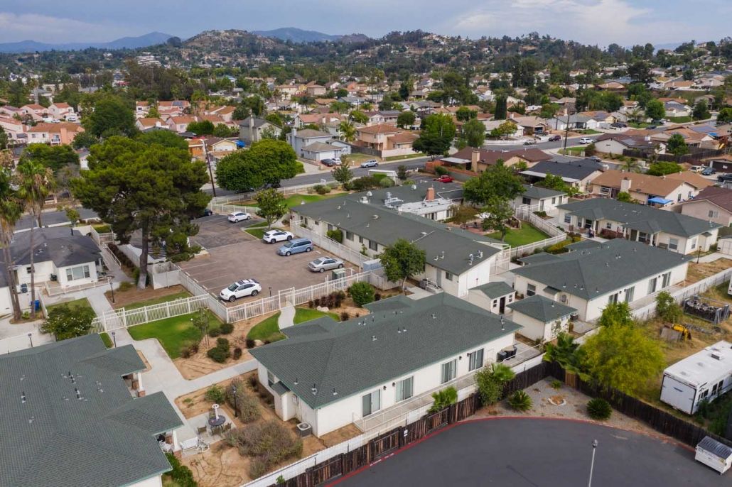 Aerial view of a suburban residential neighborhood with houses, cars, and surrounding hills.