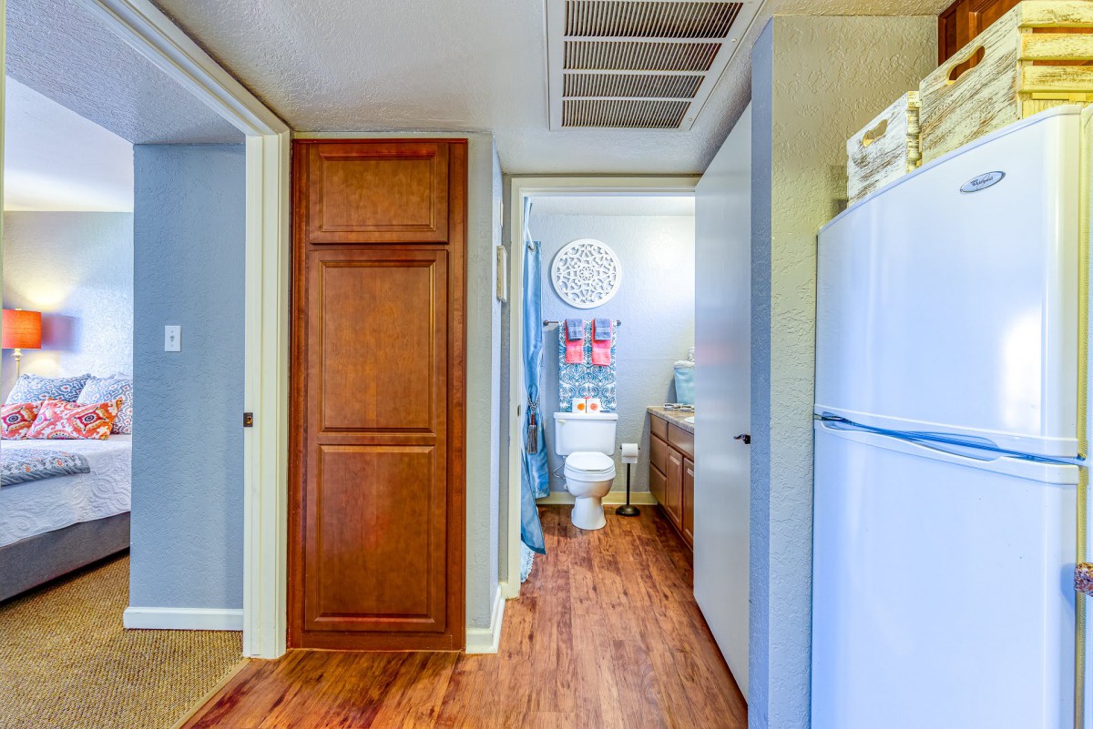 A hallway leading to a bathroom with wood flooring and adjacent kitchen area.