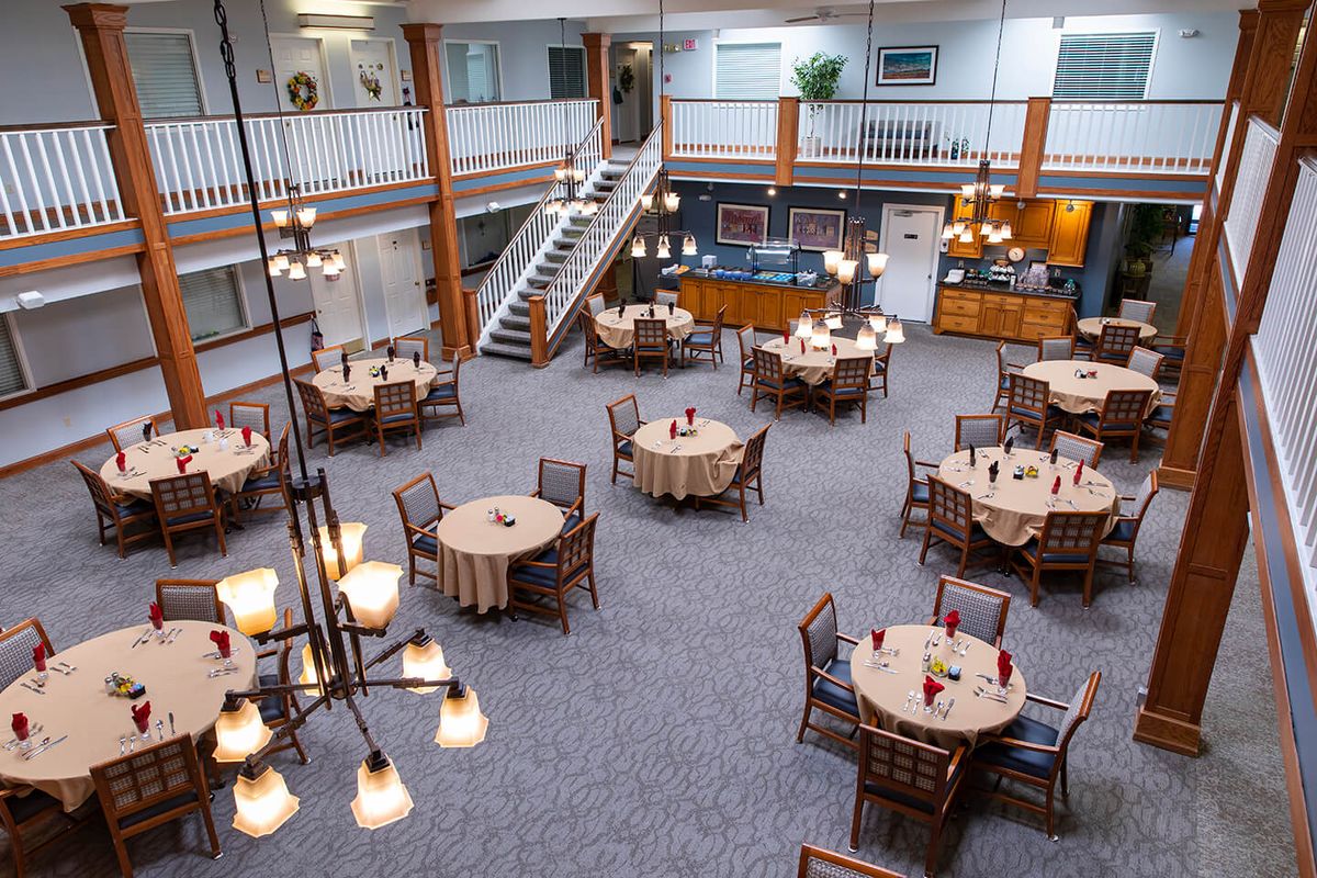 An overhead view of a spacious dining area with round tables set for guests, featuring a large chandelier and an elegant staircase.