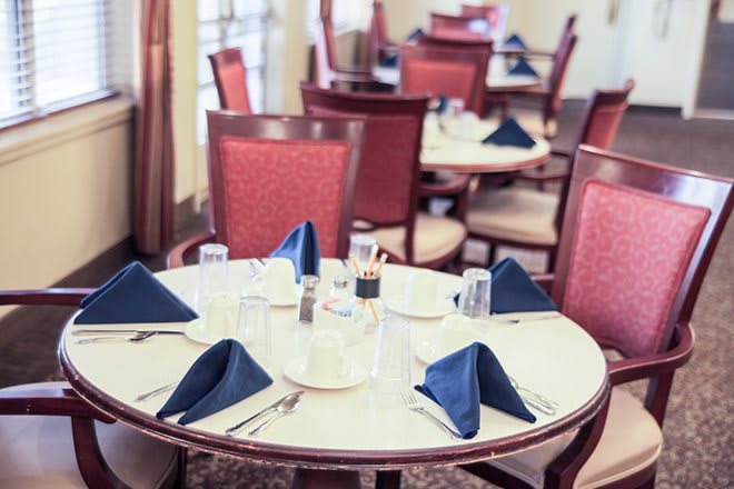 A neatly set restaurant table with blue napkins and red chairs.