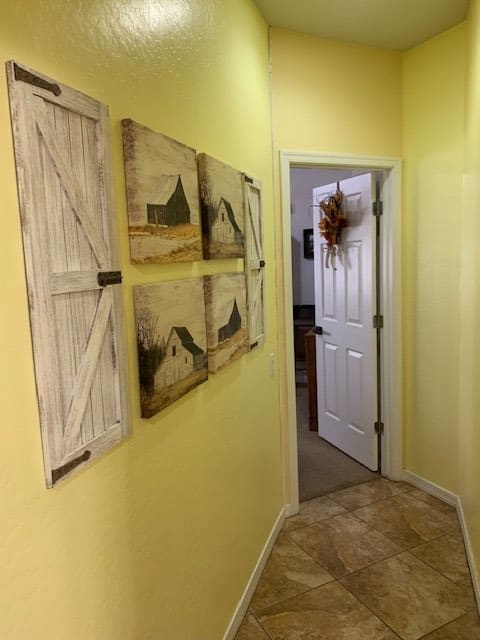 A cozy hallway with yellow walls, featuring decorative barn-themed art and wooden shutter accents, leading to an open door.