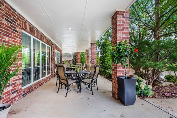 An inviting covered patio with a table and chairs surrounded by brick columns and lush greenery.