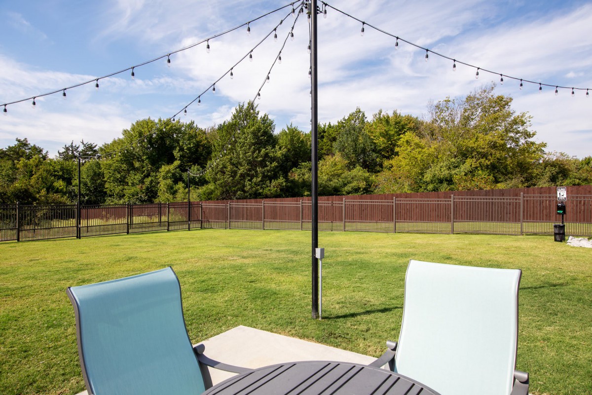 A cozy outdoor patio with string lights, overlooking a grassy lawn and surrounded by trees.
