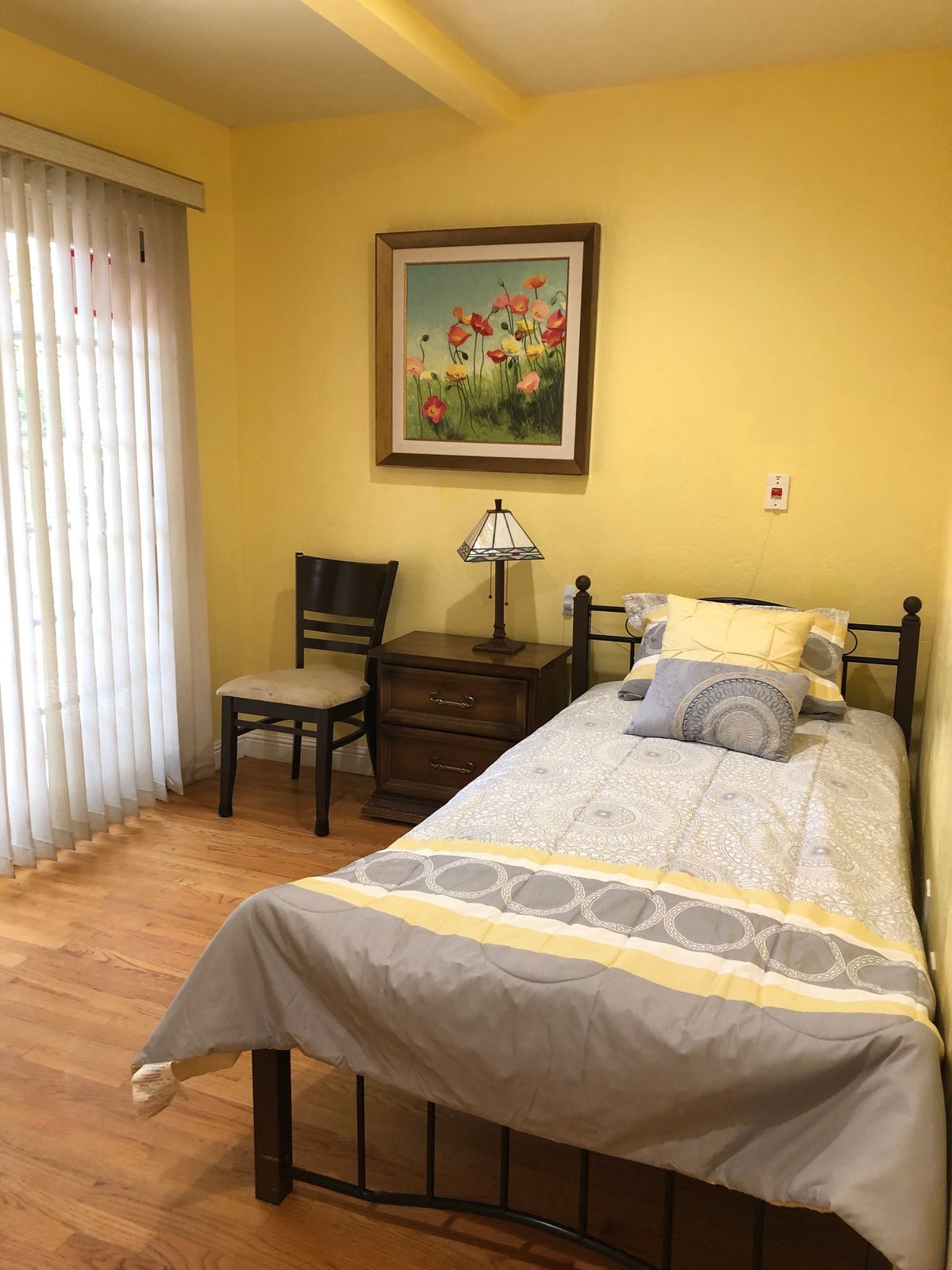 A cozy bedroom with a single bed, yellow walls, and a window with curtains.