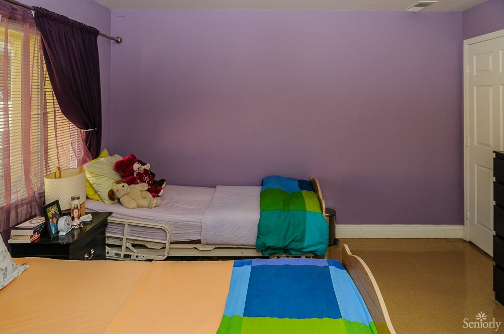 A bedroom with two neatly made beds, featuring vibrant bedspreads and a set of stuffed animals on one bed against a purple wall.