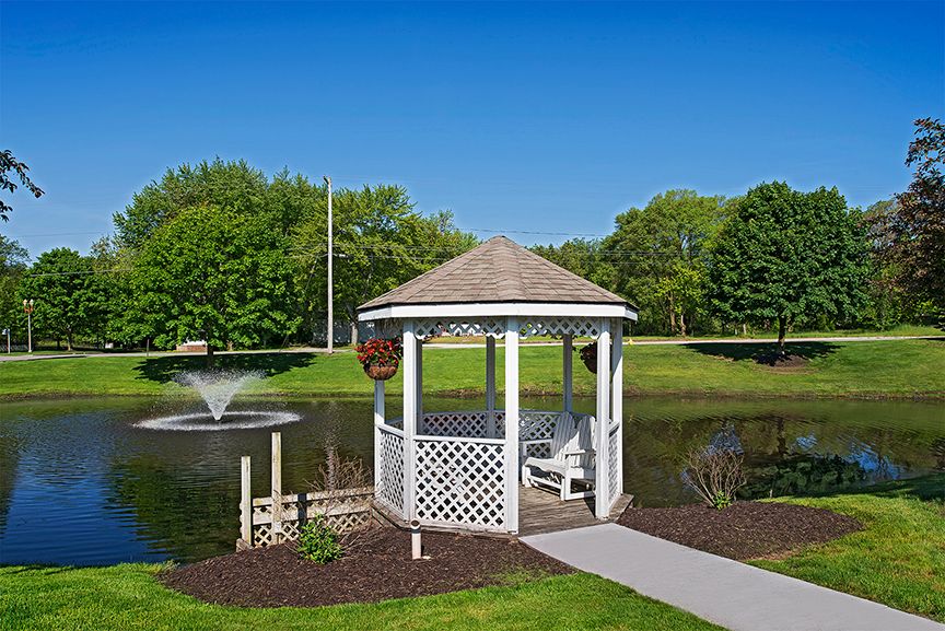 A serene gazebo by a pond with a fountain surrounded by lush greenery.