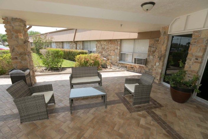 A covered outdoor patio with wicker furniture and a garden view.