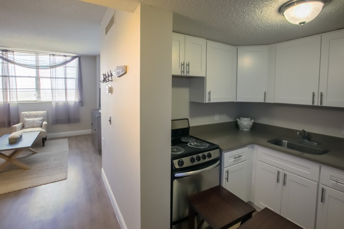A compact apartment kitchen with white cabinets and a modern stove, adjacent to a bright living area.