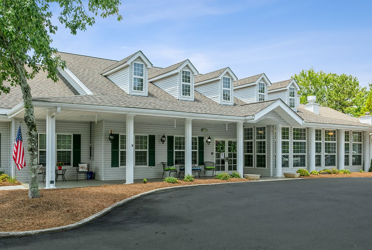 A residential-style building with a porch and multiple dormer windows, surrounded by trees.