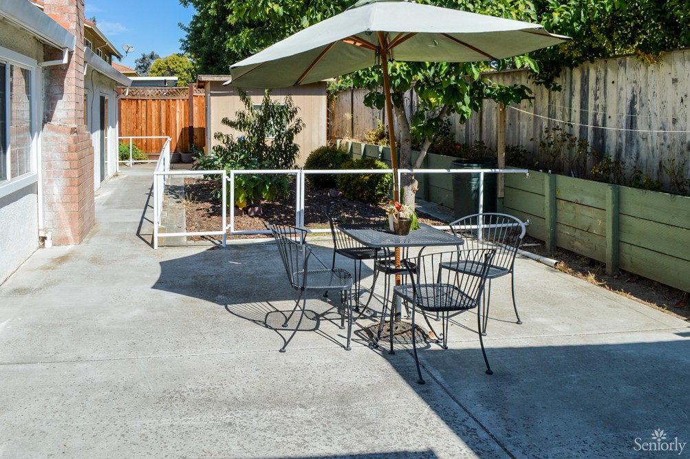 A sunny outdoor patio with a table, chairs, and an umbrella.