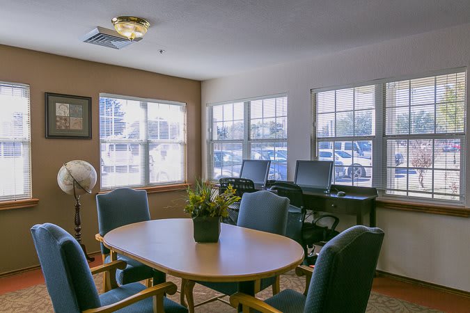 A well-lit meeting room with a conference table, chairs, and computer desks by the windows.