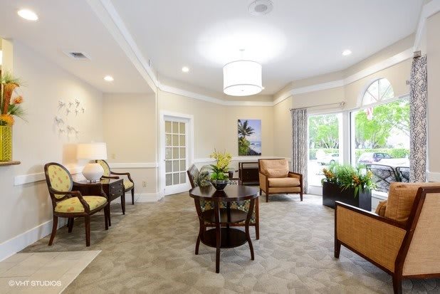 A cozy living room with comfortable chairs, a central table, and natural light streaming through large windows.
