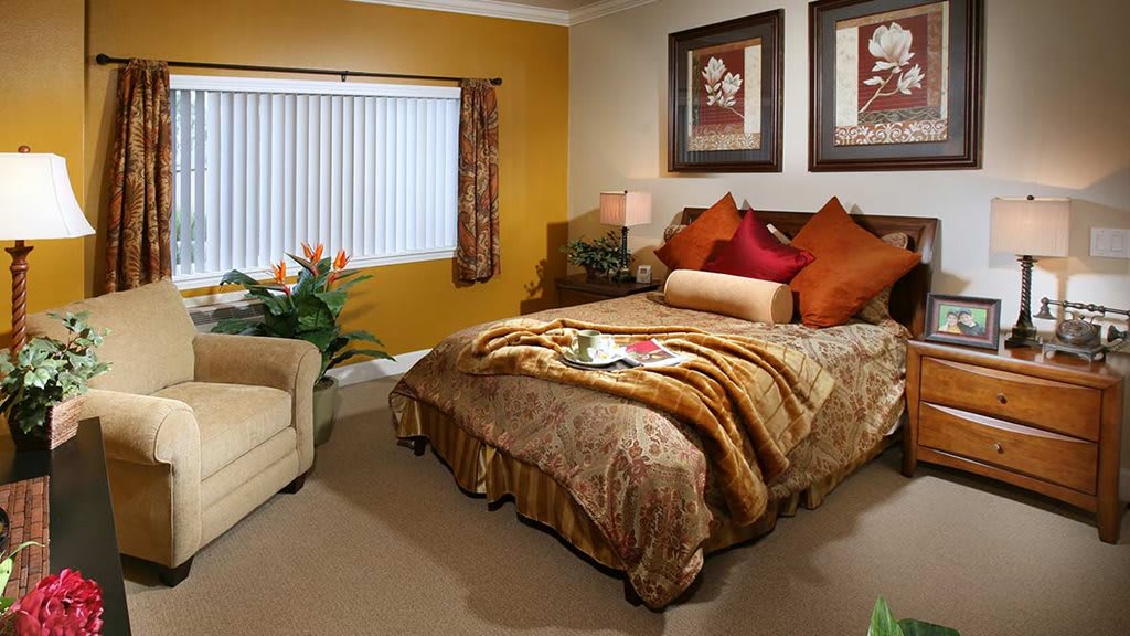 A cozy bedroom with warm color tones, featuring a comfortable bed adorned with decorative pillows and blankets. Two pieces of artwork hang above the bed, enhancing the room's inviting atmosphere.