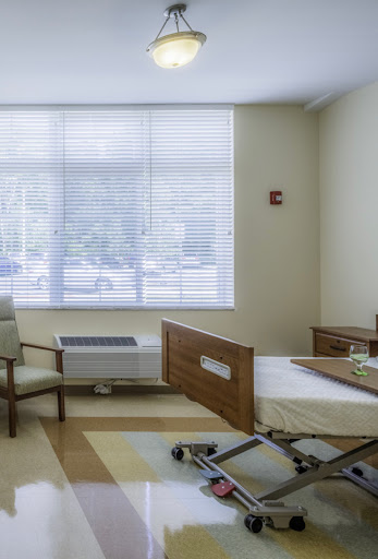 A well-lit hospital patient room featuring a bed and seating area.