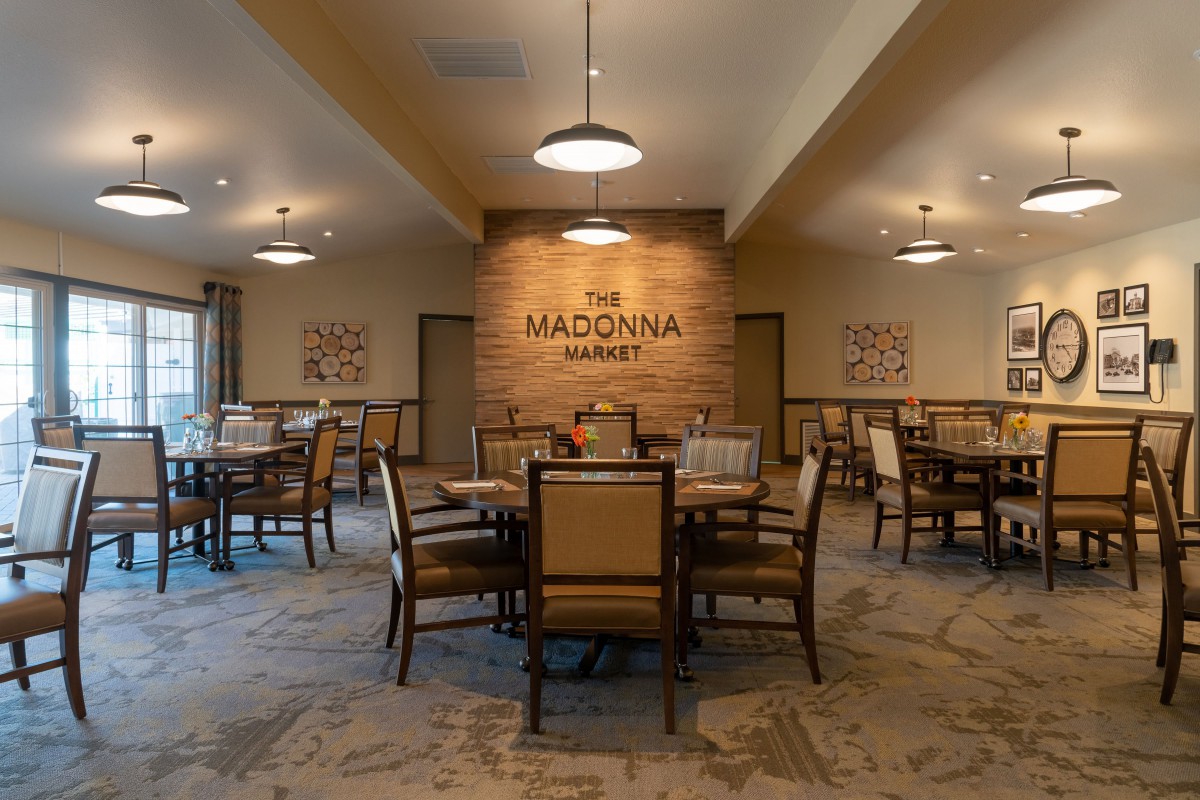 A cozy dining room interior with tables and chairs arranged under warm lighting, featuring a brick wall backdrop.