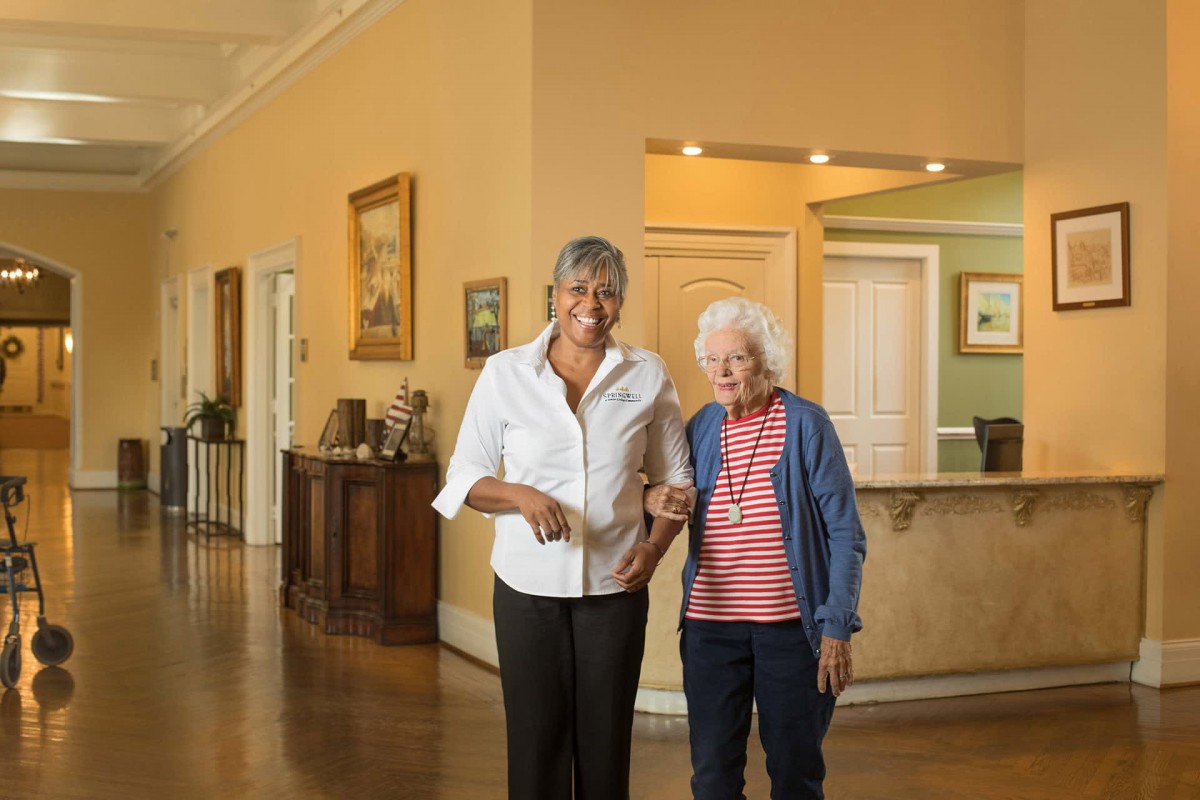 A caregiver assists an elderly woman inside a warm and inviting home environment.