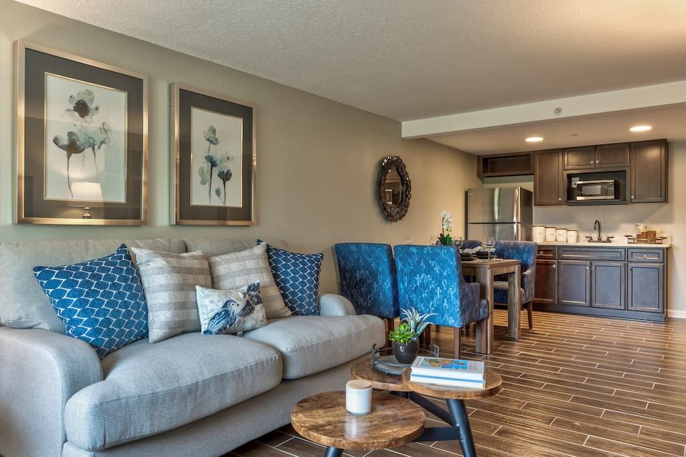 A modern living room with a cozy sofa, colorful cushions, and a stylish coffee table, extending into an open kitchen and dining area.