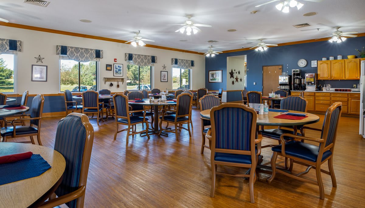 A spacious dining area with wooden floors, tables, and chairs, decorated with artwork and large windows.