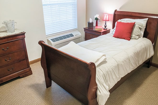 A cozy bedroom with a wooden single bed, nightstand, and a window.