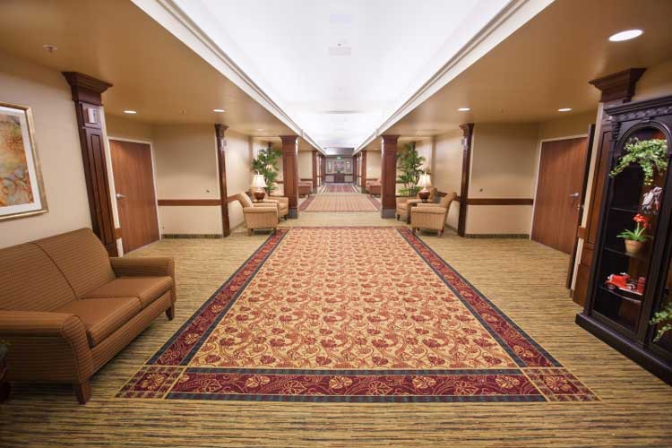 A hotel hallway with patterned carpet and seating areas.