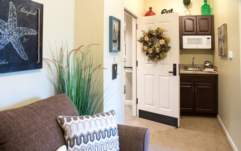 A cozy living space featuring a decorative wreath on the door, with a view into a kitchenette adorned with charming decor.