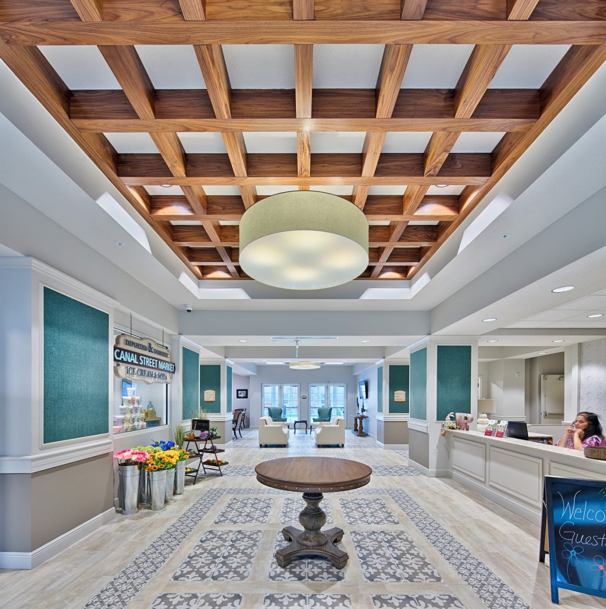 A modern lobby with a wooden ceiling and stylish lighting fixture, featuring a central table and decorative rug.