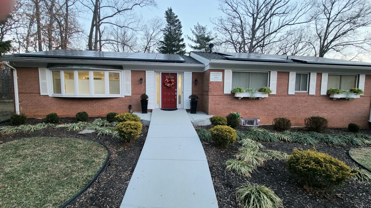 A brick house with a well-maintained front yard and a red door, featuring a concrete pathway leading to the entrance.