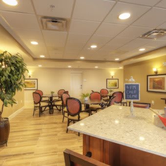 A well-lit meeting room with tables and chairs, featuring decorative plants and framed artwork on the walls.