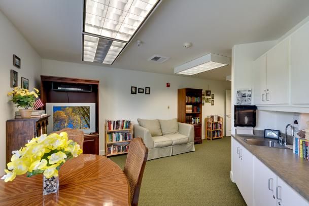 A cozy office space featuring a sofa, bookshelf, table with chairs, and decorative artwork.
