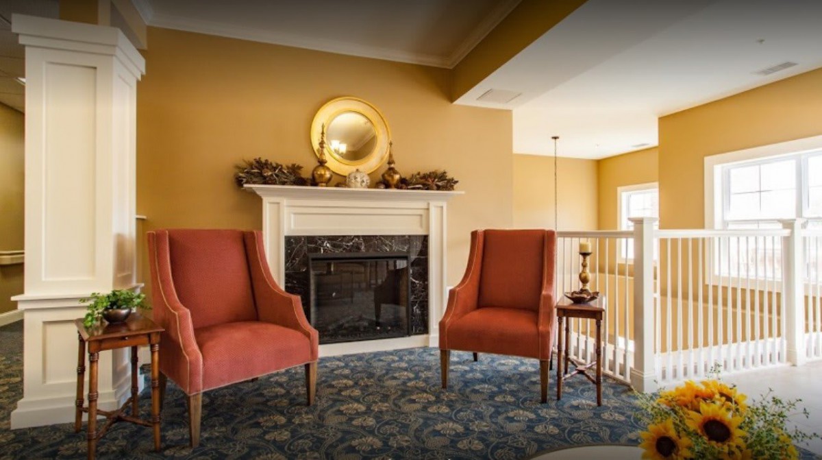 A cozy living room with two red chairs flanking a decorative fireplace, adorned with a round mirror and autumn accents.