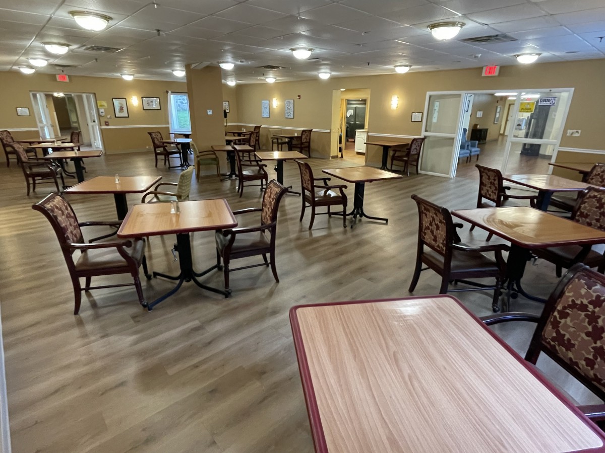 An empty dining area with wooden tables and chairs, illuminated by ceiling lights.
