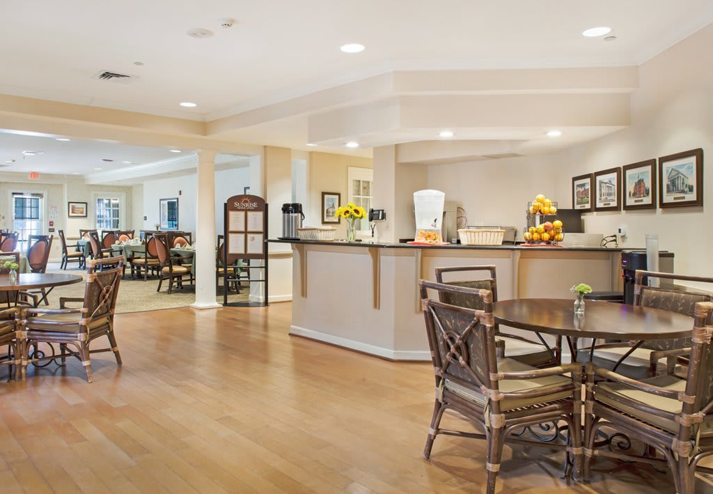 A spacious cafe with wooden floors and bright lighting, featuring several tables and chairs.