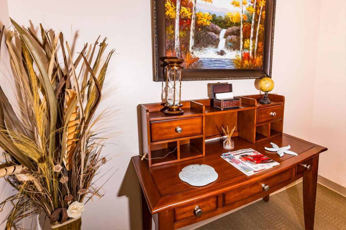 A well-organized wooden desk with decorative items and a painting on the wall.