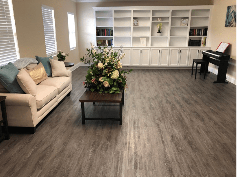 A spacious living room with a beige couch, a table with floral arrangements, and white built-in bookshelves.