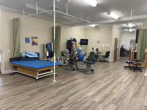 A spacious rehabilitation therapy room equipped with exercise equipment and therapy beds.