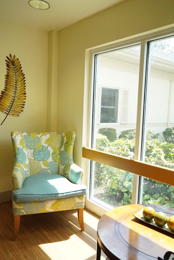 A cozy corner featuring a floral armchair illuminated by natural light, adjacent to a large window with views of greenery.