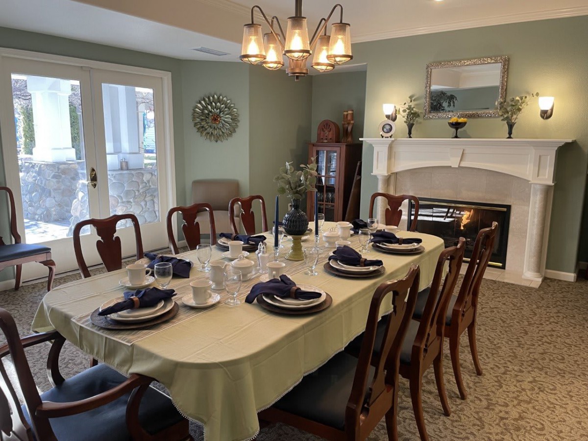 A well-set dining room table with a chandelier above and a fireplace in the background.