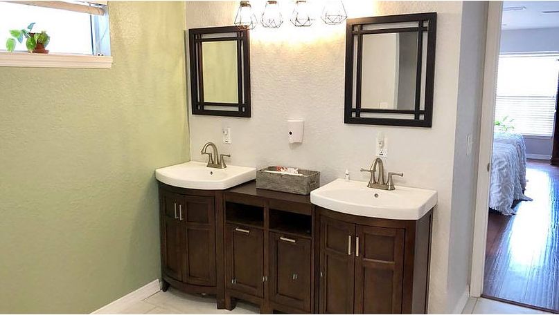 A modern bathroom with double sinks, stylish mirrors, and a central lighting fixture.