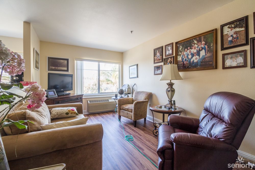 A cozy living room with comfortable seating, a large window, and framed pictures on the wall.
