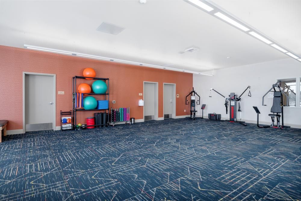 A well-lit fitness room with various exercise equipment and yoga balls.