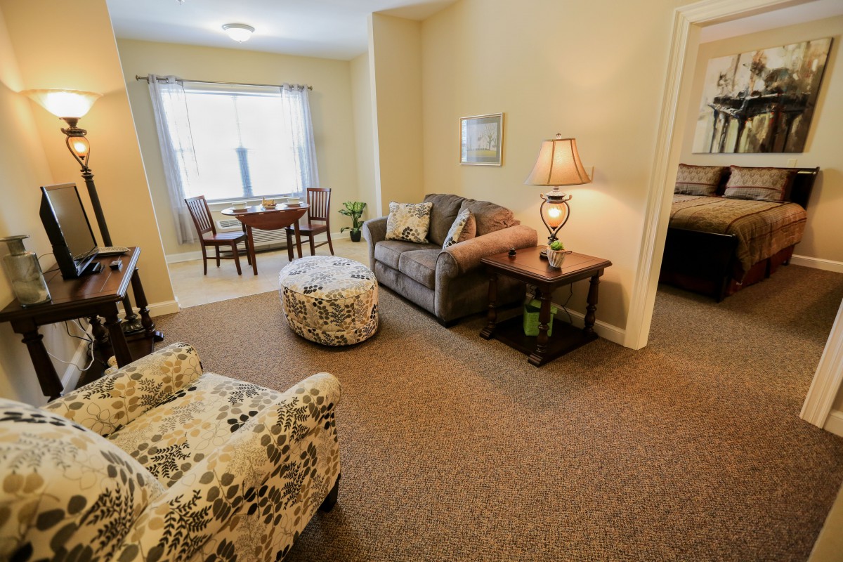 A cozy living room with a sofa, armchair, and a dining area in the background.