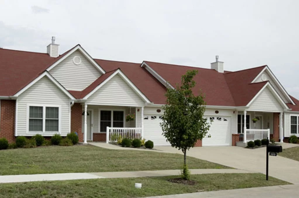 A suburban duplex with red roofs and white siding, featuring garages and a small front yard.