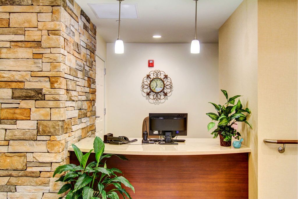 A modern office reception area with a wooden desk, plants, and a wall-mounted clock.