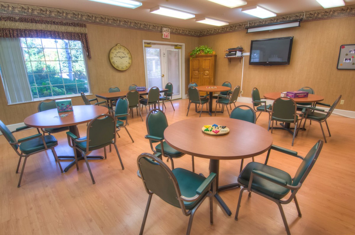 A well-lit meeting room with round tables, chairs, and a wall-mounted television.