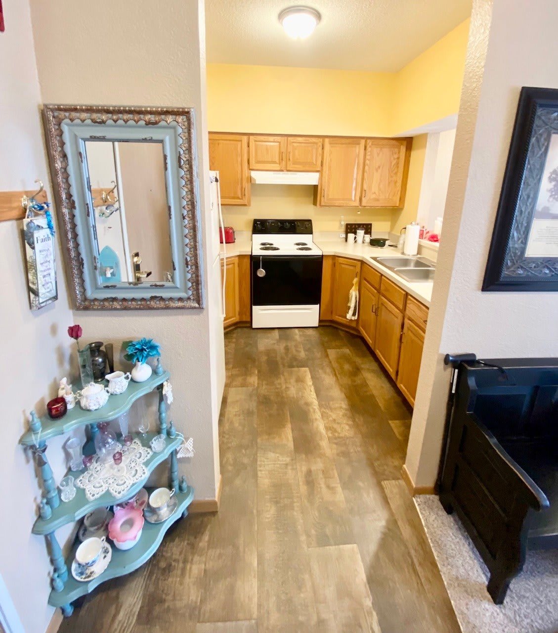 A cozy kitchen with wooden cabinets and a decorative mirror, featuring a small shelf with teacups.